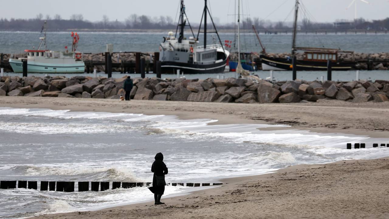 Eine Spaziergängerin ist bei grauem Wetter am Ostseestrand unterwegs.