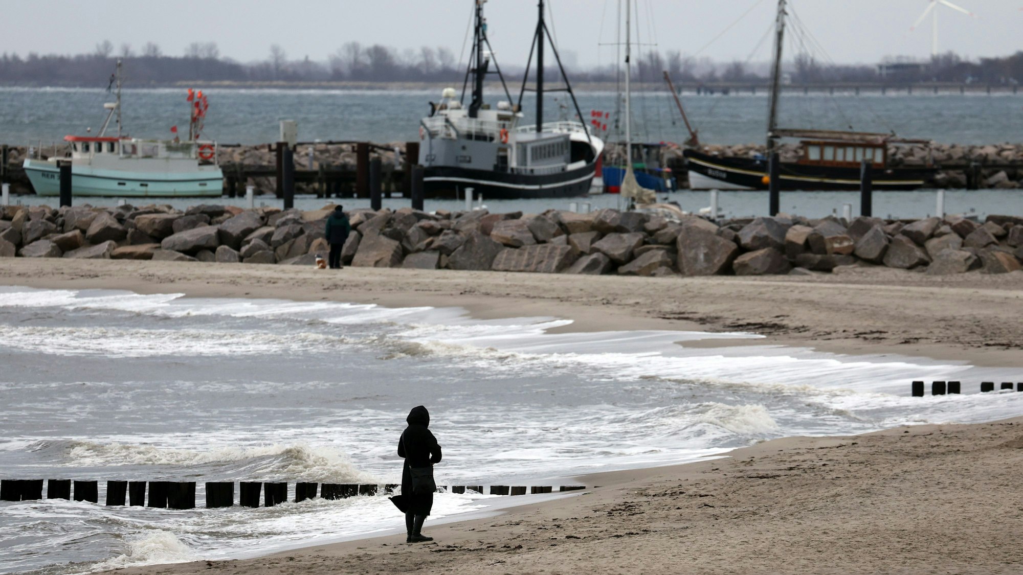 Eine Spaziergängerin ist bei grauem Wetter am Ostseestrand unterwegs.