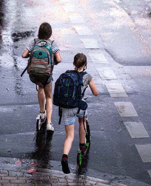 Zwei Schulkinder sind in Köln auf ihren Tretrollern unterwegs.