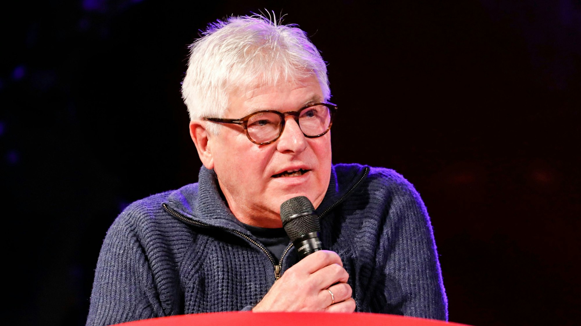 Axel Molinski, Geschäftsführer der Volksbühne am Rudolfplatz, mit Mikrofon auf der Bühne.