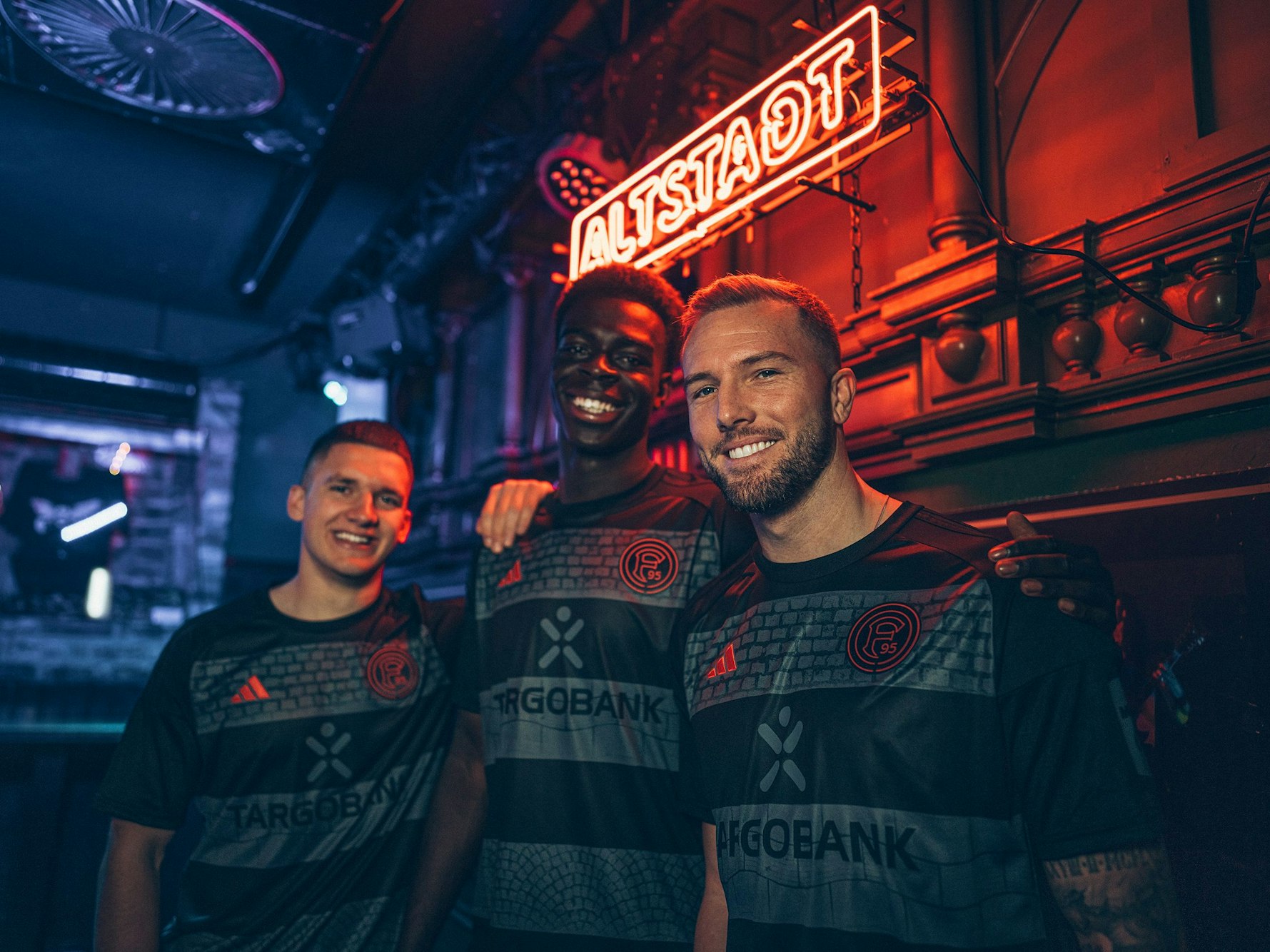 Die Düsseldorf-Profis Christos Tzolis, Joshua Quarshie und Andre Hoffmann (v.l.) posieren im Sonder-Trikot „Altstadt“.