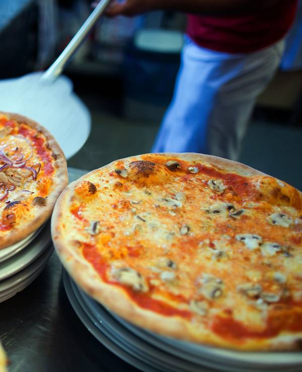 In einer Pizzeria liegen fertige Pizzen auf Tellern.
