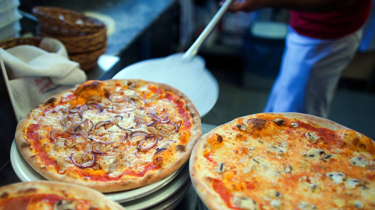 In einer Pizzeria liegen fertige Pizzen auf Tellern.