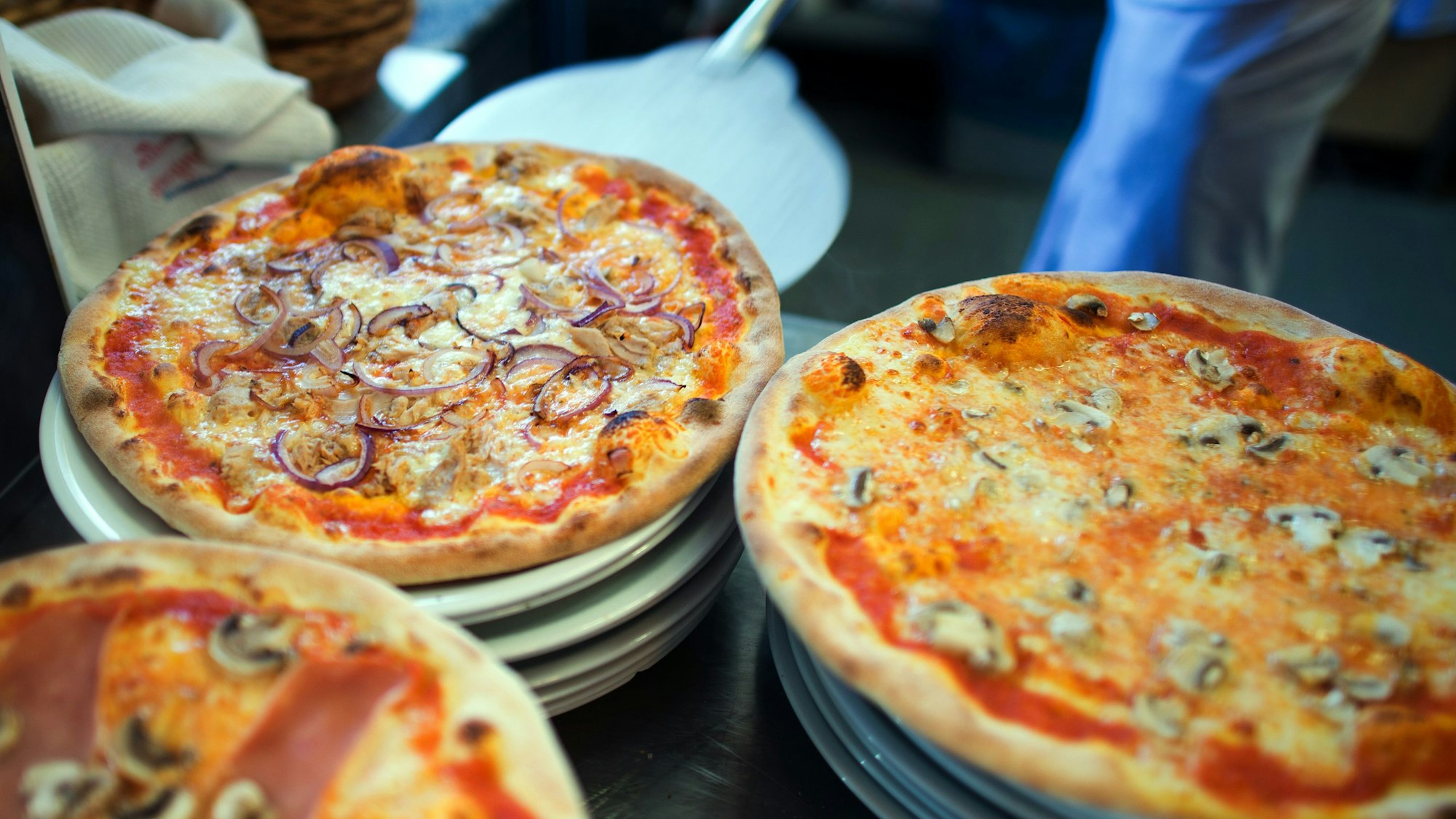In einer Pizzeria liegen fertige Pizzen auf Tellern.