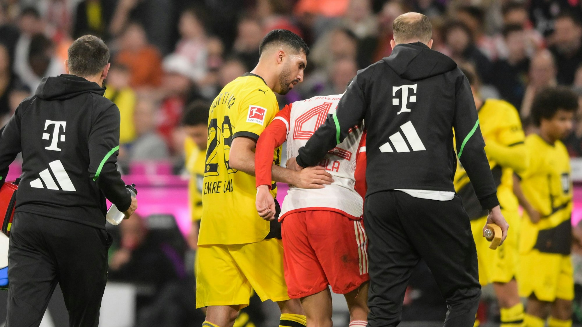 Jamal Musiala humpelt gestützt von einem Bayern-Betreuer und BVB-Kapitän Emre Can vom Platz.