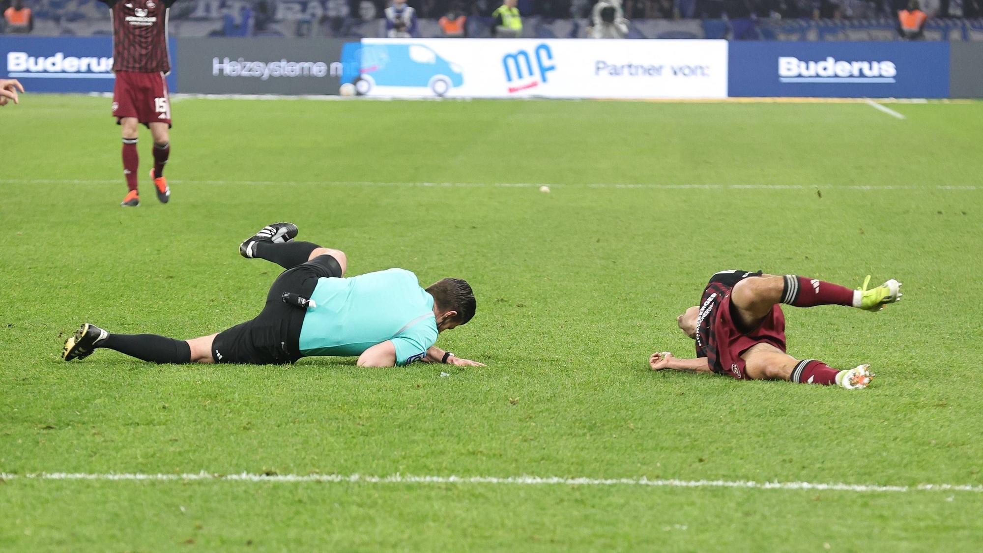 Nach dem heftigen Zusammenprall im Zweitliga-Topspiel in Berlin liegen Schiedsrichter Alexander Sather und Jens Castrop vom 1. FC Nürnberg am Boden.