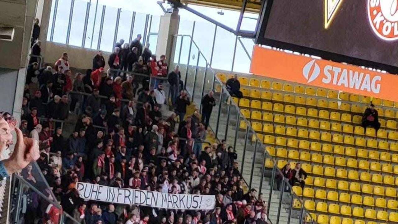 In einem Stadion halten Fans im Zuschauerblock ein Banner mit der Aufschrift „Ruhe in Frieden Markus!“ hoch.