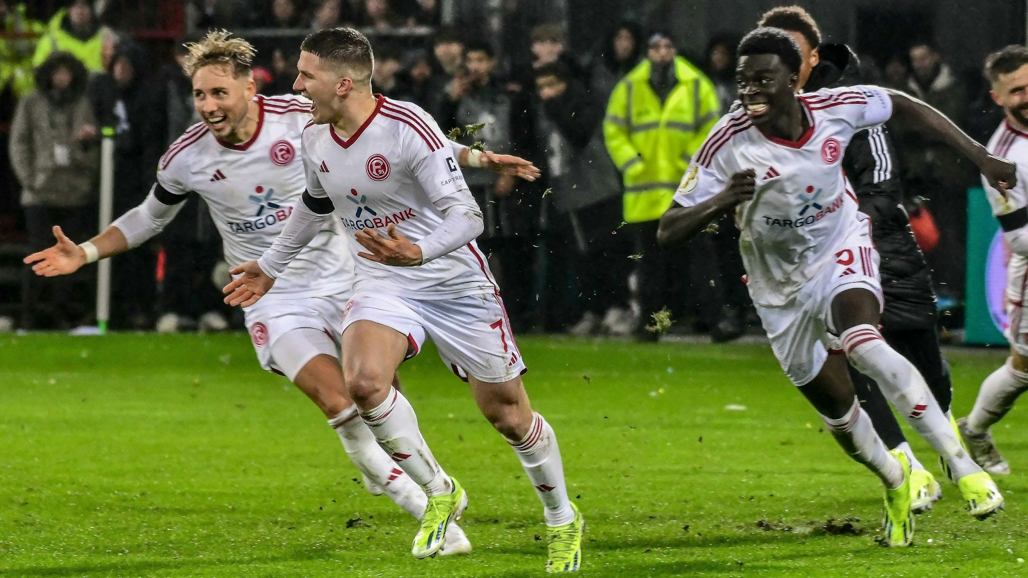 Christos Tzolis hat den Elfmeter zum Sieg eingenetzt und jubelt mit Jona Niemiec und Joshua Quarshie von Fortuna Düsseldorf.