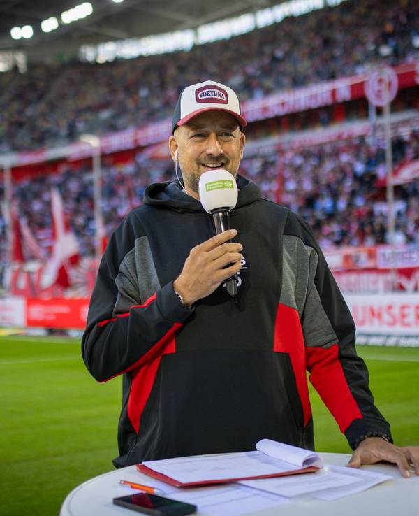 Für Fortuna Düsseldorfs Stadionsprecher André Scheidt steht mit Mikrofon an einem Pult.