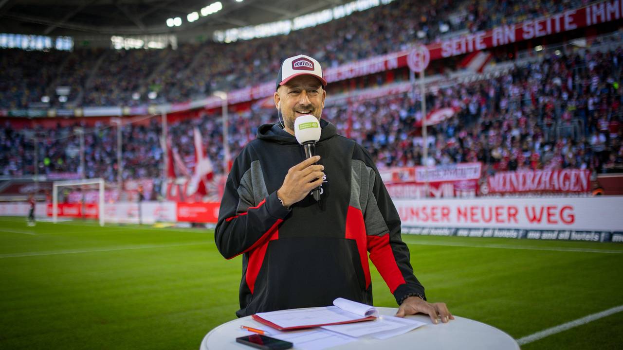Für Fortuna Düsseldorfs Stadionsprecher André Scheidt steht mit Mikrofon an einem Pult.