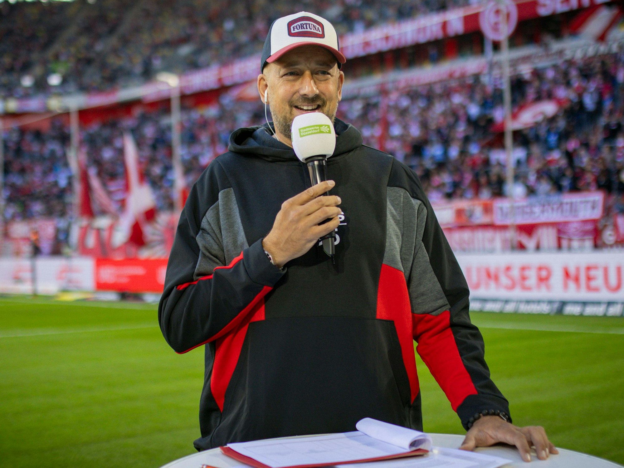 Für Fortuna Düsseldorfs Stadionsprecher André Scheidt steht mit Mikrofon an einem Pult.