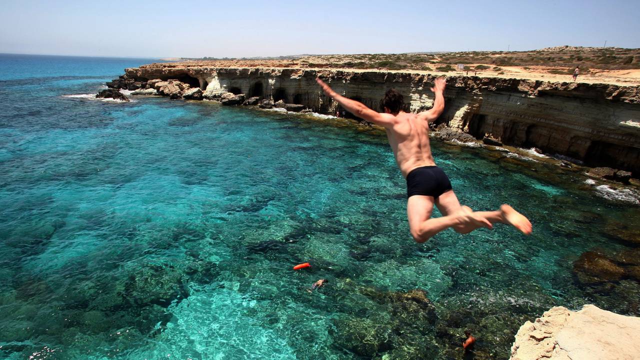 Ein Mann springt am Cape Greco auf Zypern ins Meer.