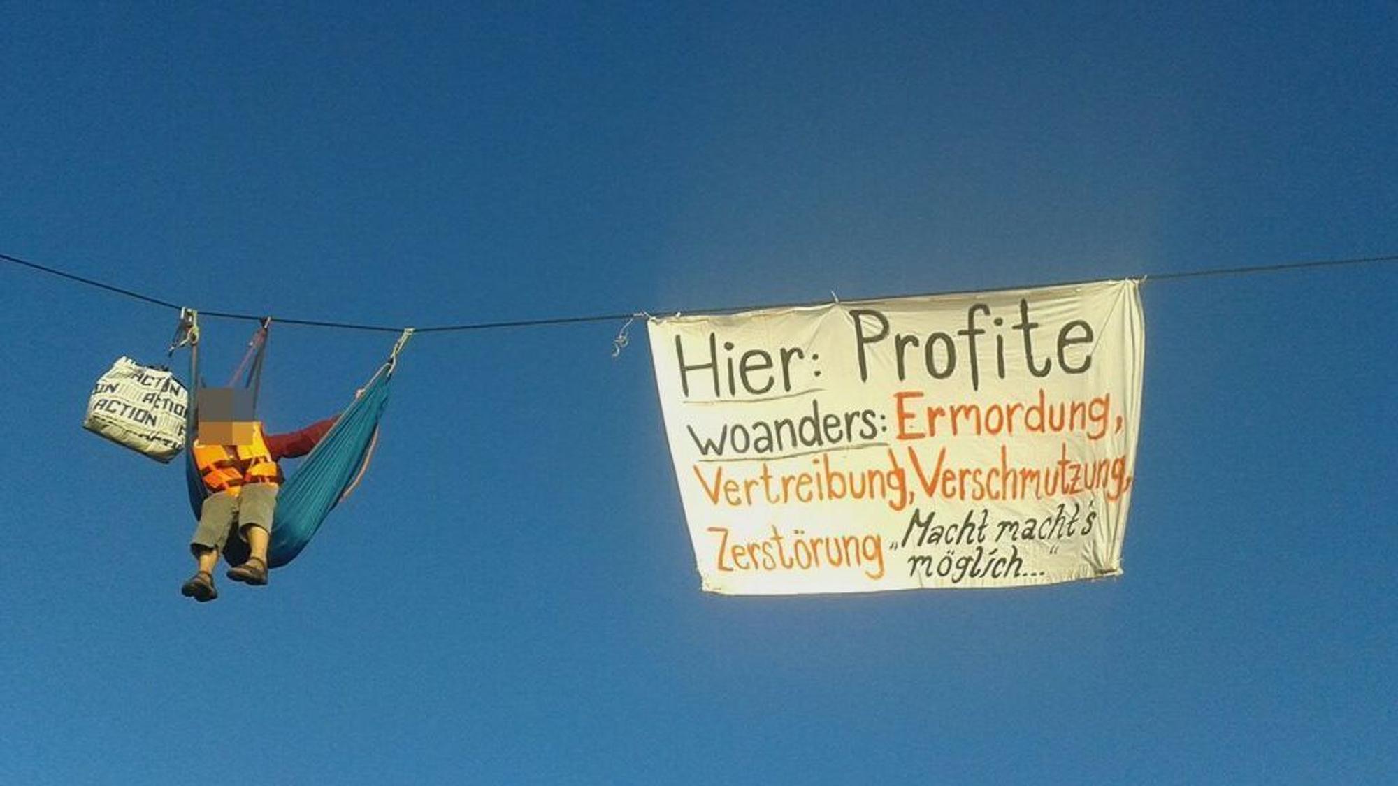 An einem Seil hängt eine Hängematte, in der eine Frau sitzt. Daneben hängt ein Banner.