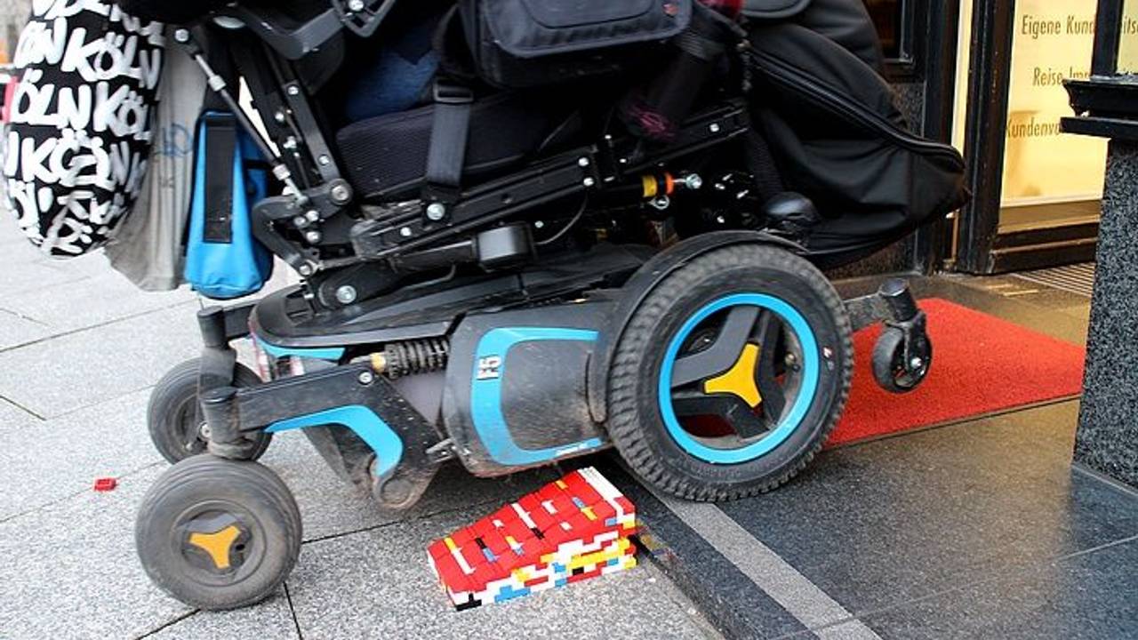 Ein Rollstuhl fährt über eine Legorampe in ein Geschäft.