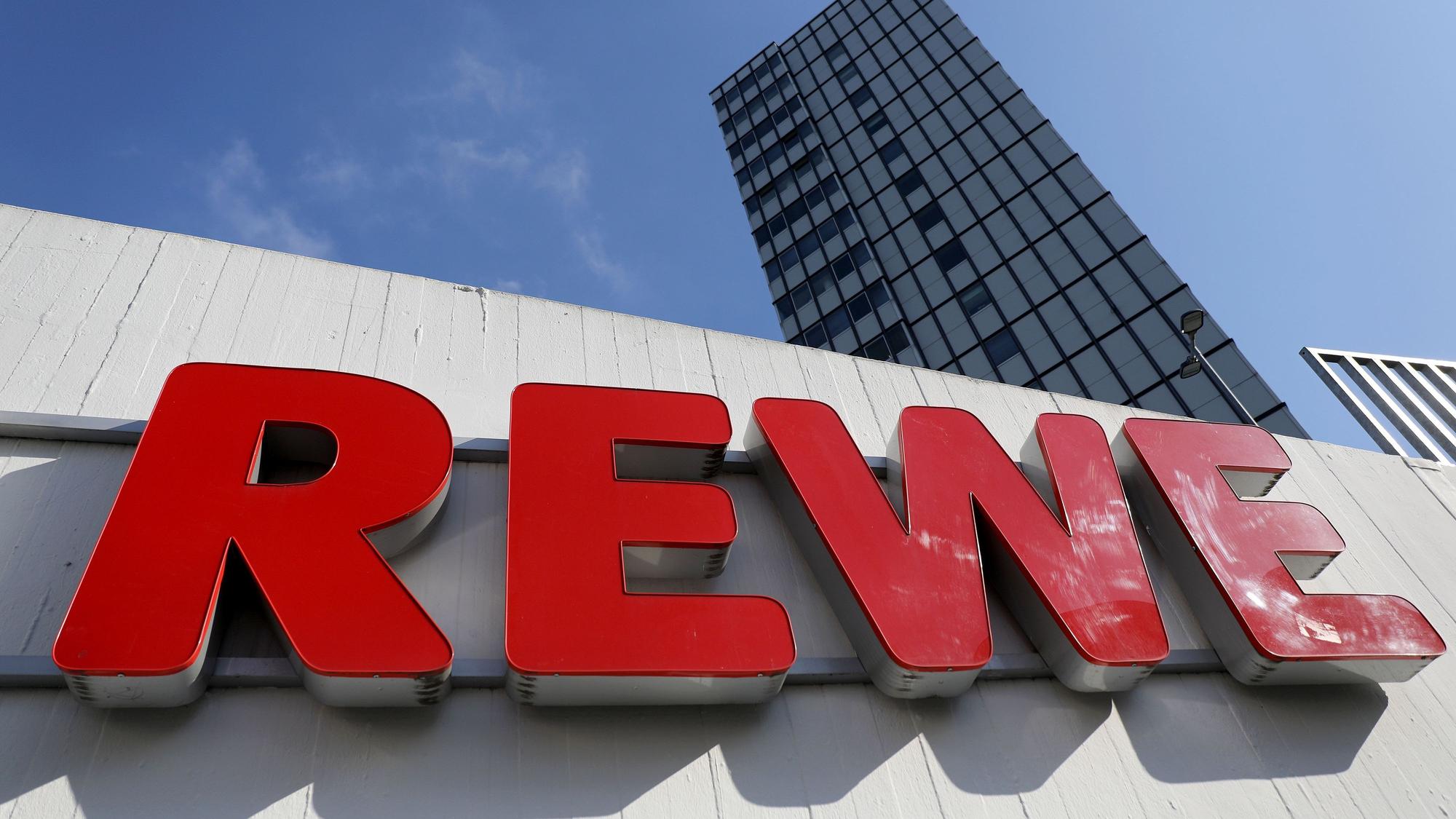 Ein Rewe Schriftzug hängt vor einem Supermarkt.