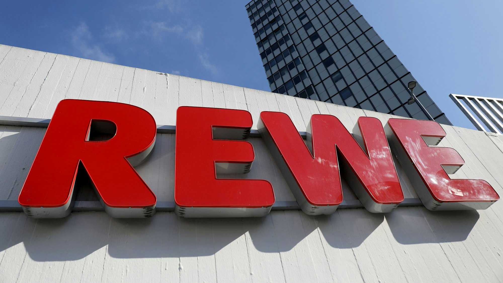 Ein Rewe Schriftzug hängt vor einem Supermarkt.