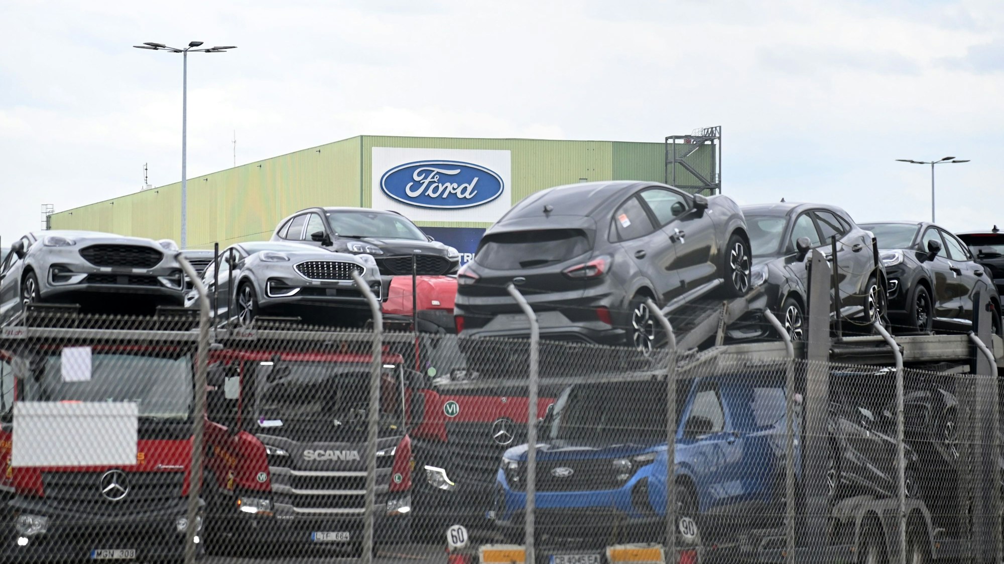 Transporter mit geladenen Autos stehen vor einem Ford-Gebäude.