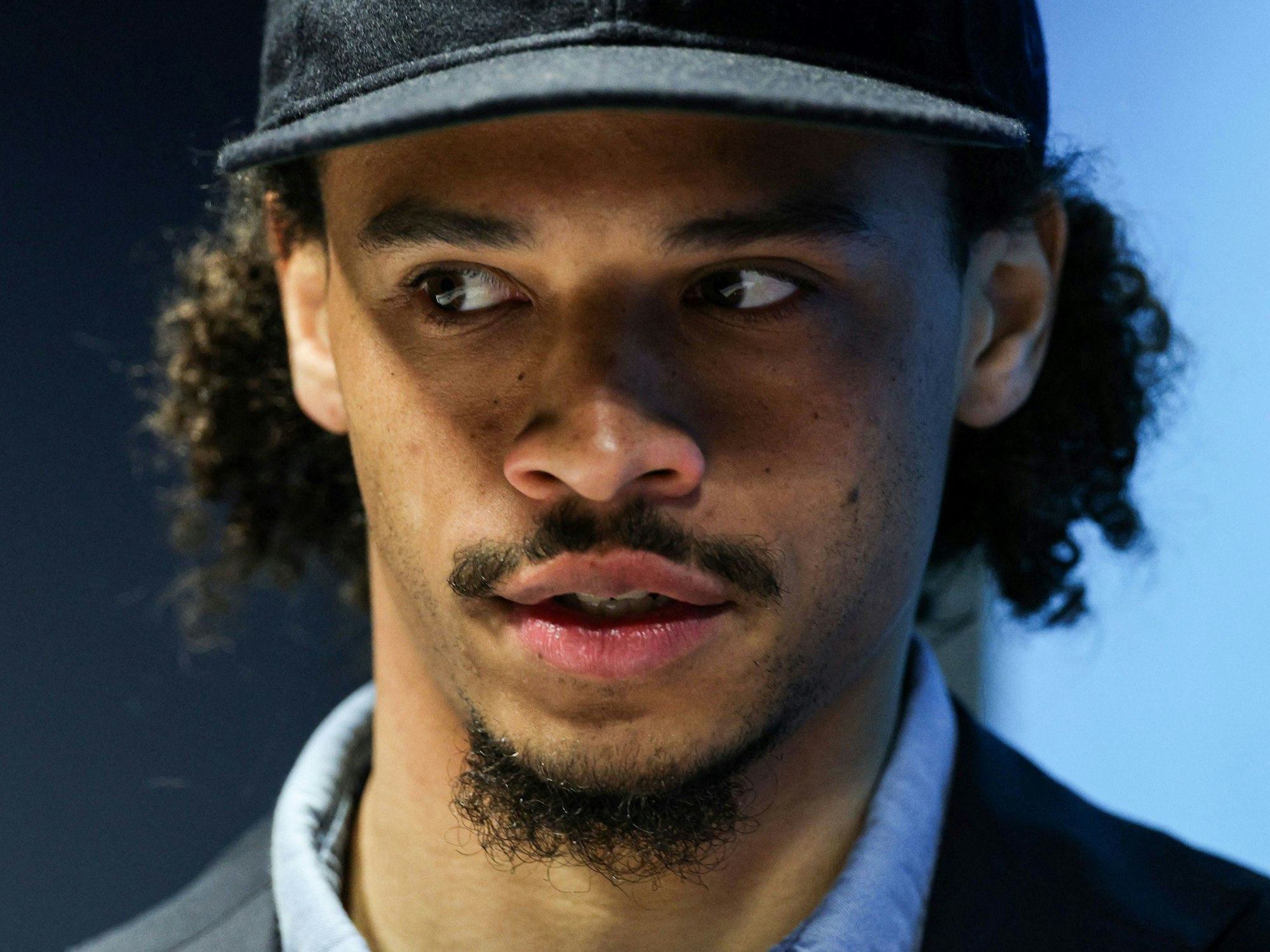 Leroy Sané kommt mit Kappe zur Pressekonferenz.