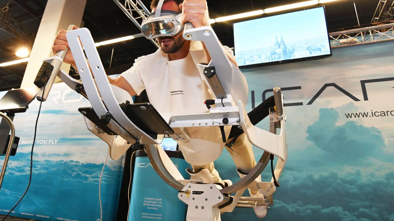 Personal Trainer Manuel Gajus liegt in Supermann-Pose auf dem ICAROS Gerät und hat eine VR-Brille an. Auf dem Bildschirm im Hintergrund sieht man den Kölner Dom.
