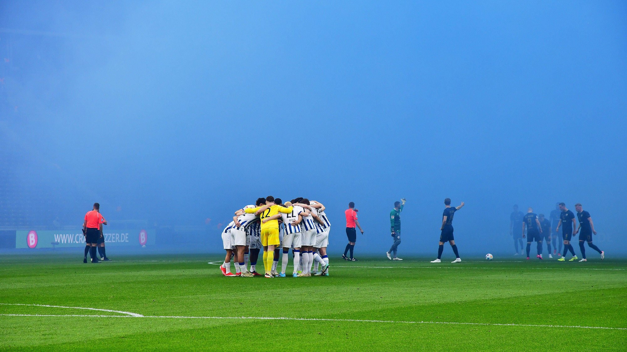 Hinter dem Berliner Spielerkreis baut sich bereits die im Rostocker Gästeblock entstandene Nebelwand auf.
