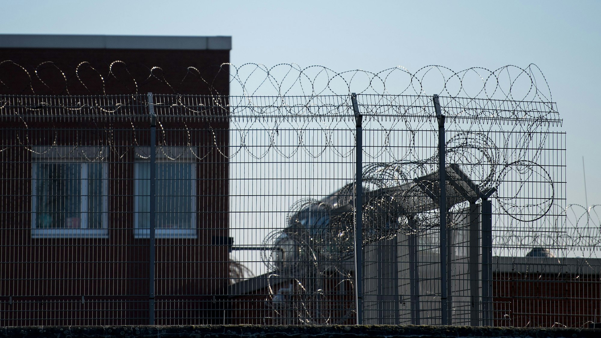Hinter einem Zaun und Stacheldraht sind Fenster der Justizvollzugsanstalt (JVA) im Stadtteil Ossendorf zu sehen.