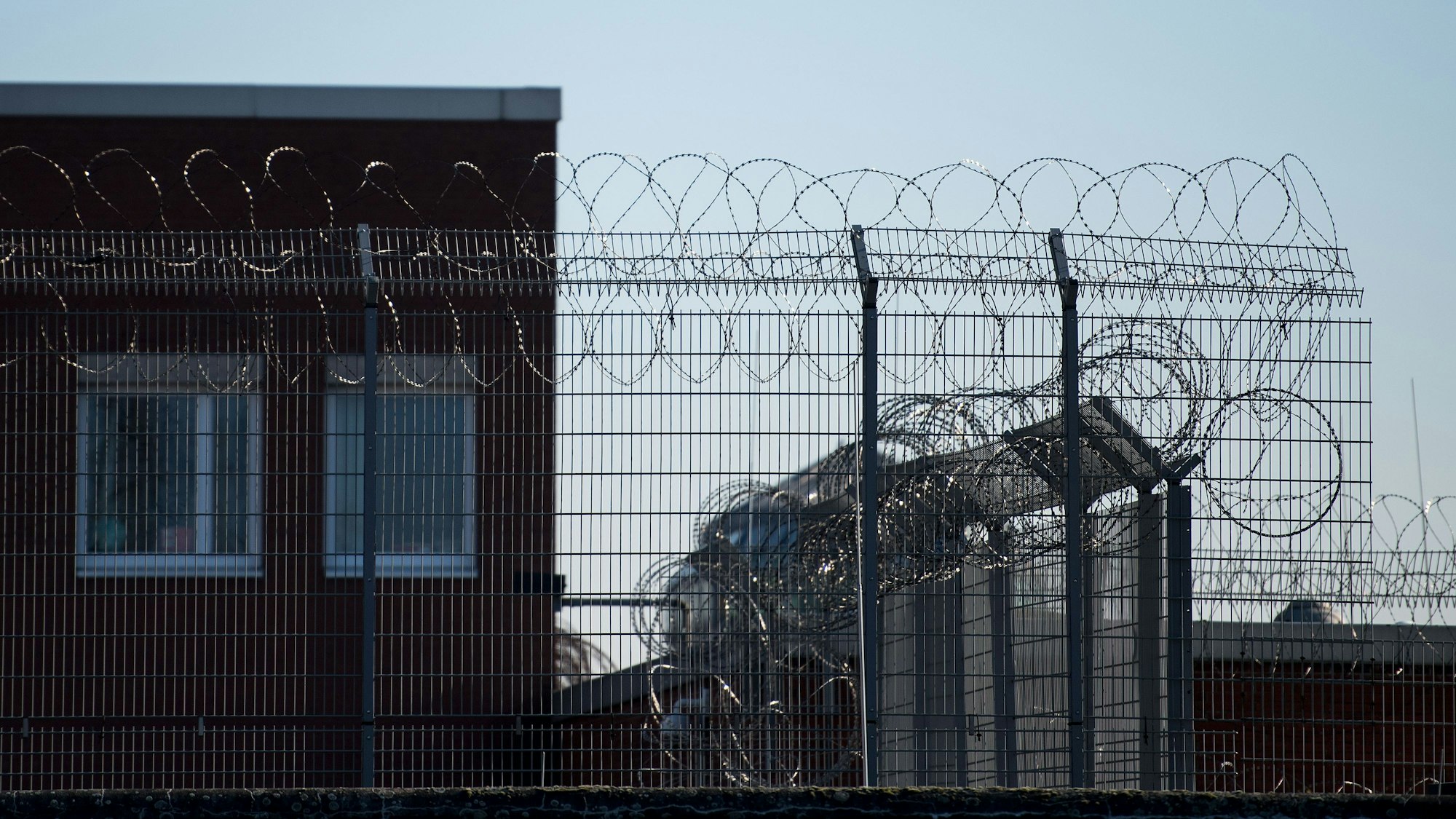 Hinter einem Zaun und Stacheldraht sind Fenster der Justizvollzugsanstalt (JVA) im Stadtteil Ossendorf zu sehen.