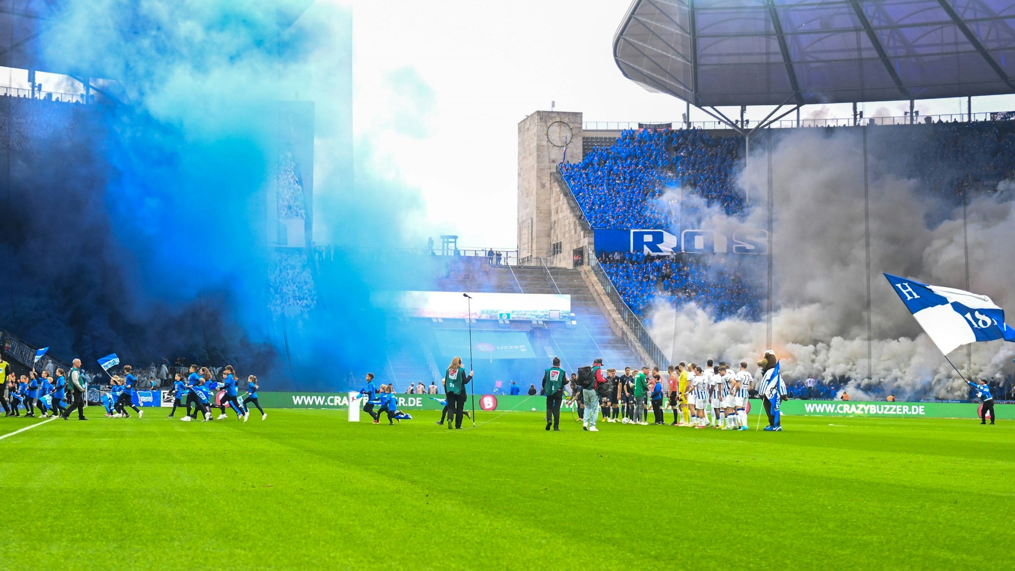 Die Mannschaften von Hertha BSC und Hansa Rostock vor dem Duell in der 2. Bundesliga. Im Hintergrund ist der aus dem Gästeblock aufsteigende Rauch zu sehen.