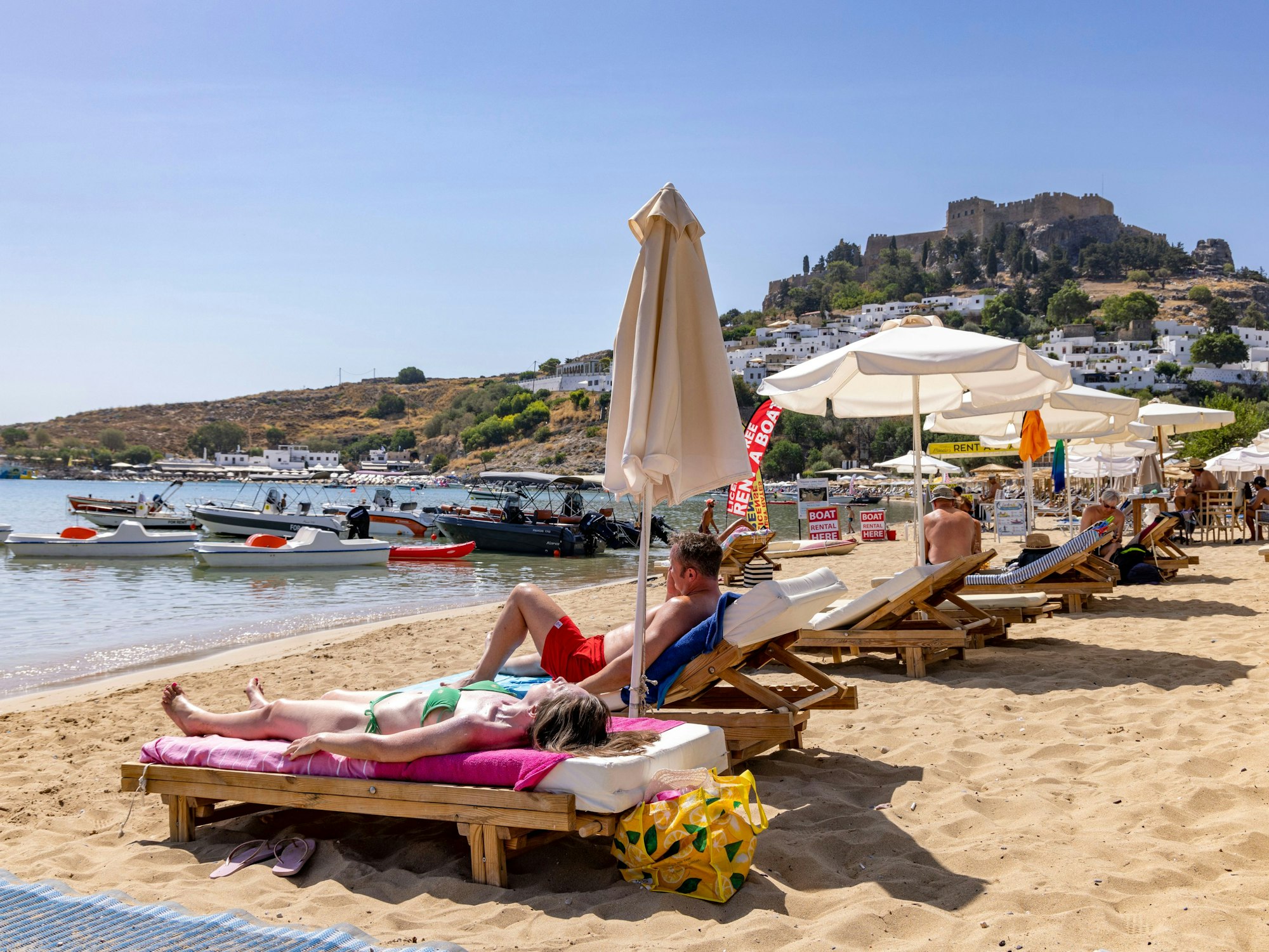 Am Strand in Lindos, etwa 10 Kilometer von den Bränden im Südosten entfernt, sind weiterhin Touristen am Strand, im Hintergrund die weltbekannte Akropolis von Lindos.