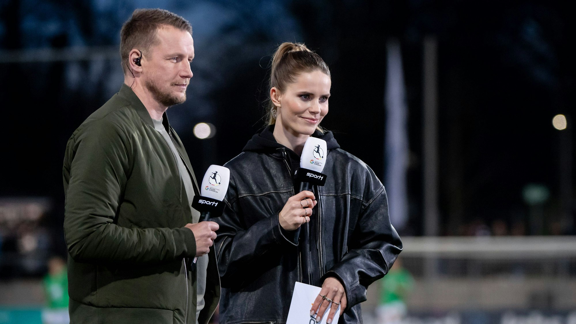 Lili Engels und Maik Franz halten bei einer Übertragung der Frauen-Bundesliga bei Sport1 Mikrofone in der Hand.