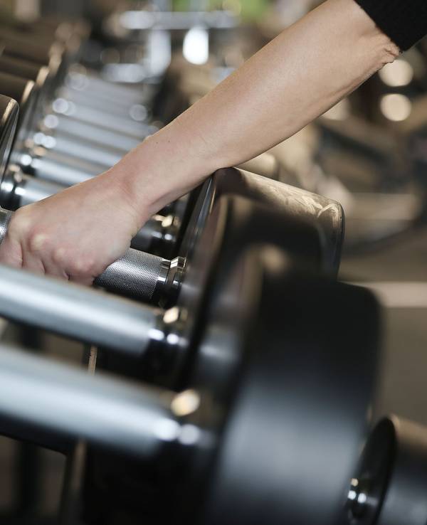 Eine Frau nimmt im Fitnessstudio Holmes Place Hanteln aus dem Ständer.
