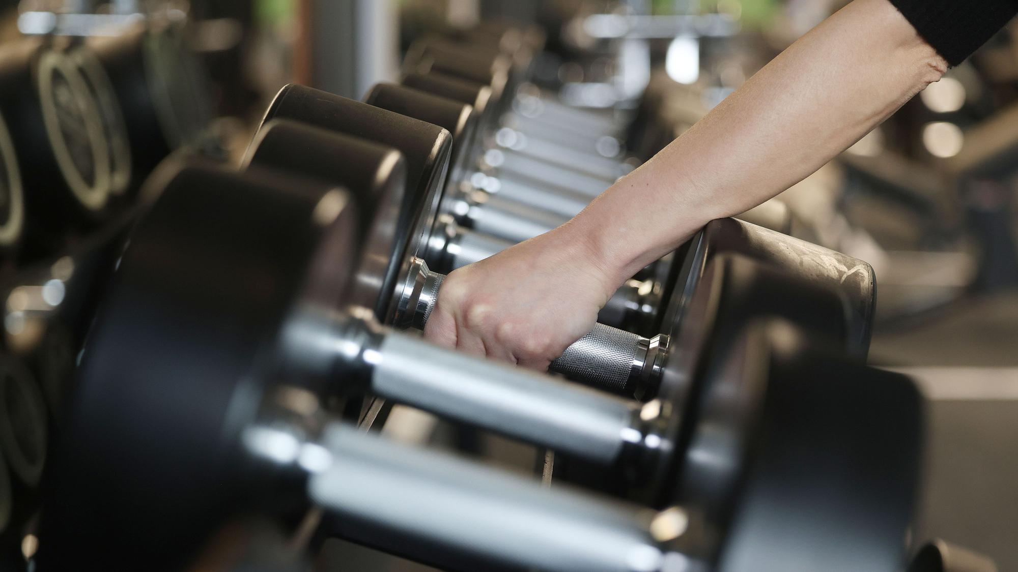 Eine Frau nimmt im Fitnessstudio Holmes Place Hanteln aus dem Ständer.