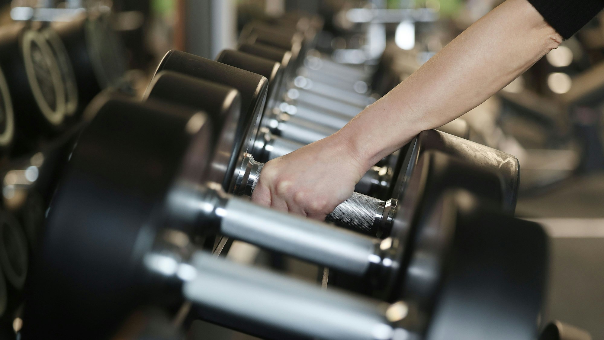 Eine Frau nimmt im Fitnessstudio Holmes Place Hanteln aus dem Ständer.