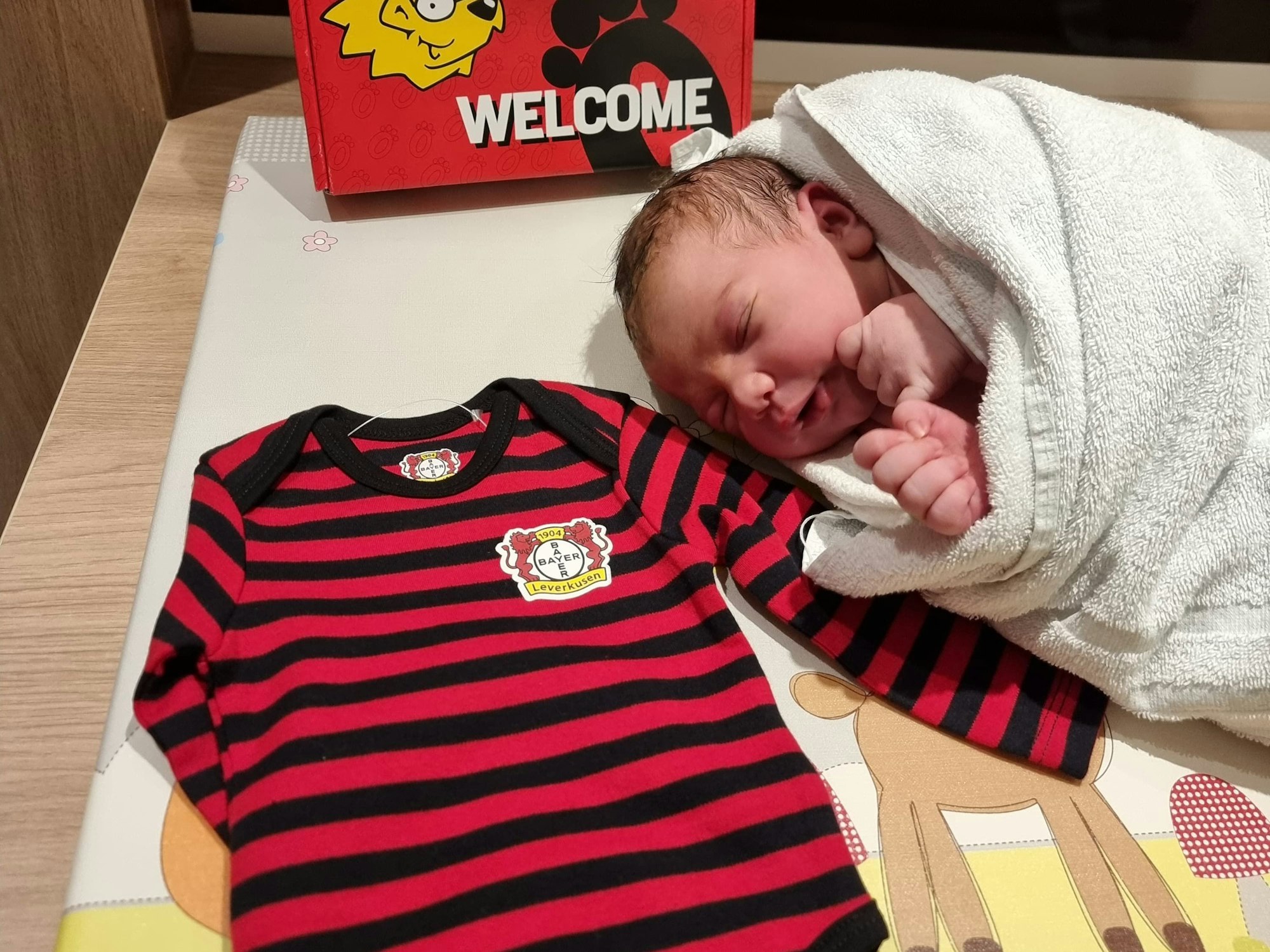 Baby liegt neben einem Strampelanzug von Bayer Leverkusen.