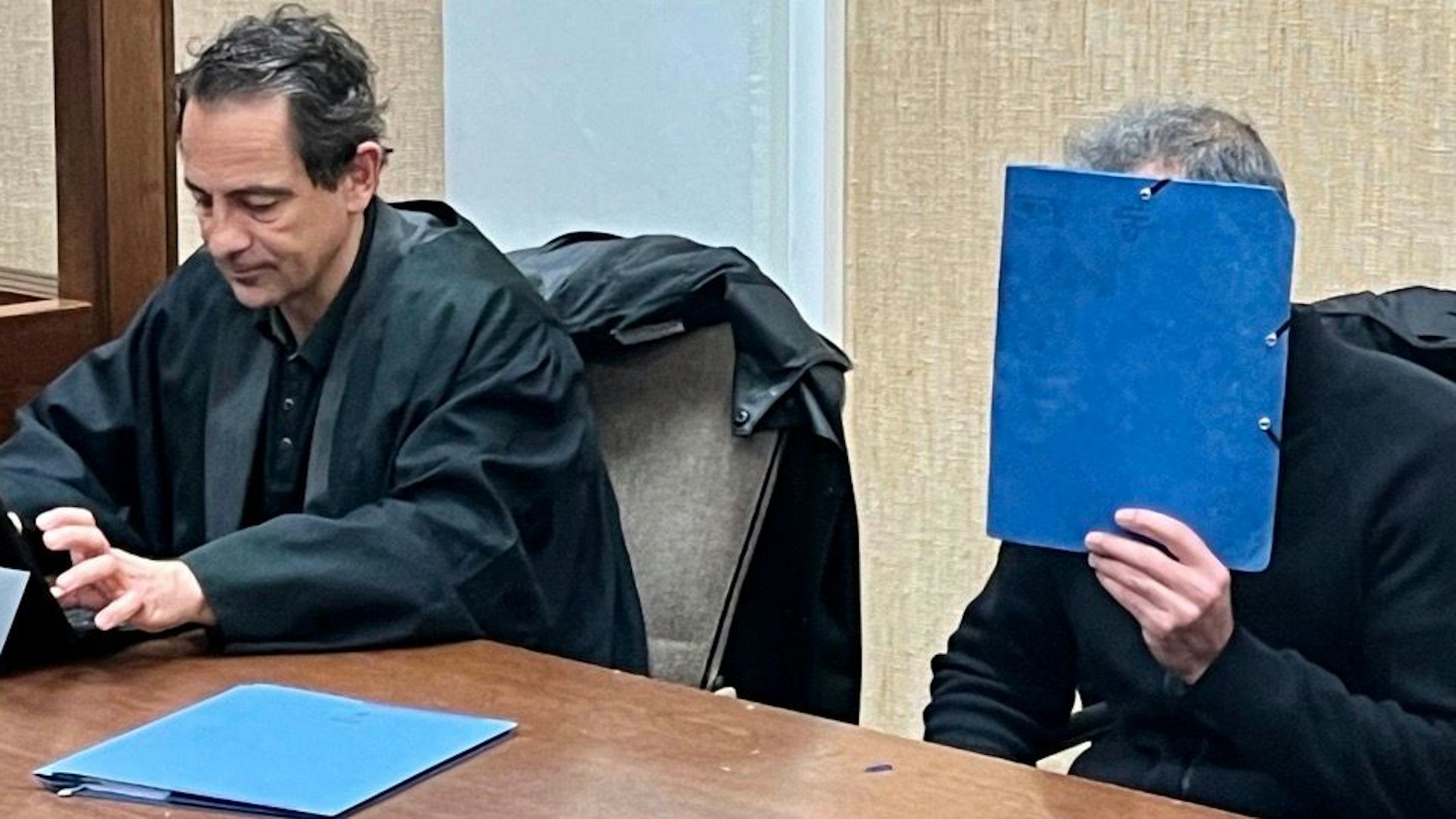 Angeklagter hält sich im Gerichtssaal einen Ordner vor das Gesicht.