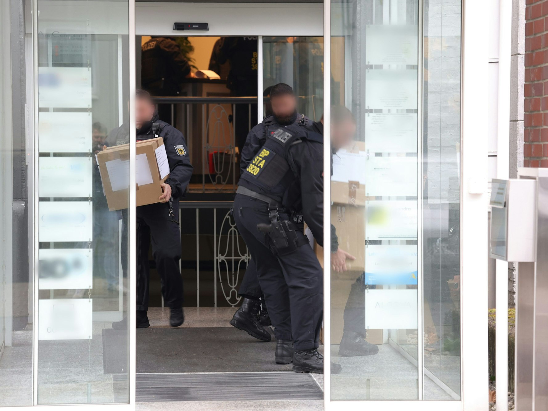 Einsatzkräfte tragen Kartons aus einem Gebäude.