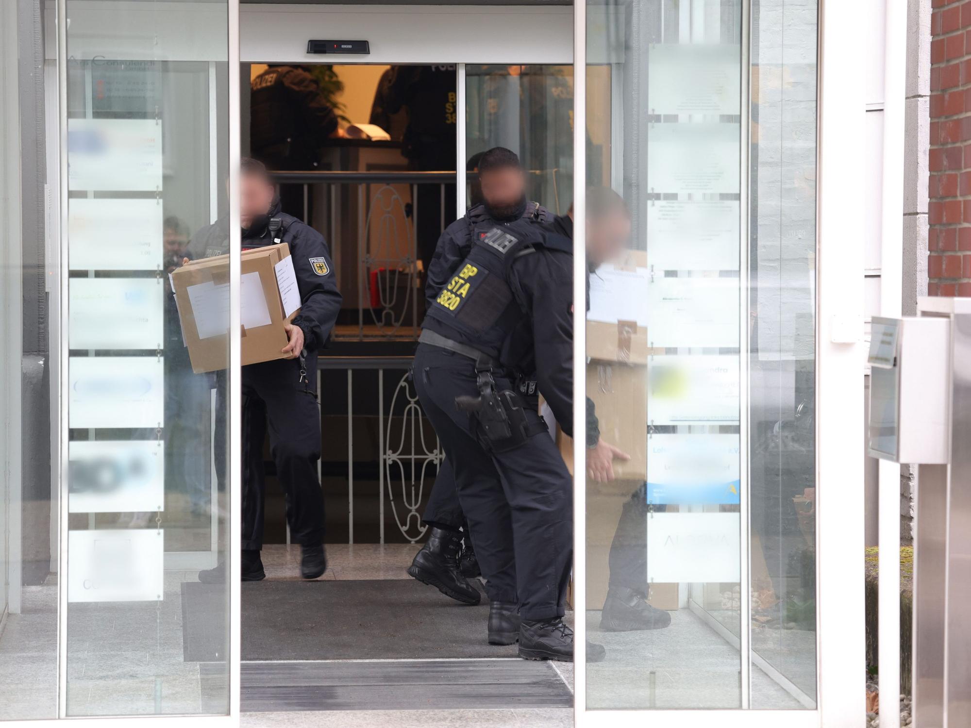 Einsatzkräfte tragen Kartons aus einem Gebäude.