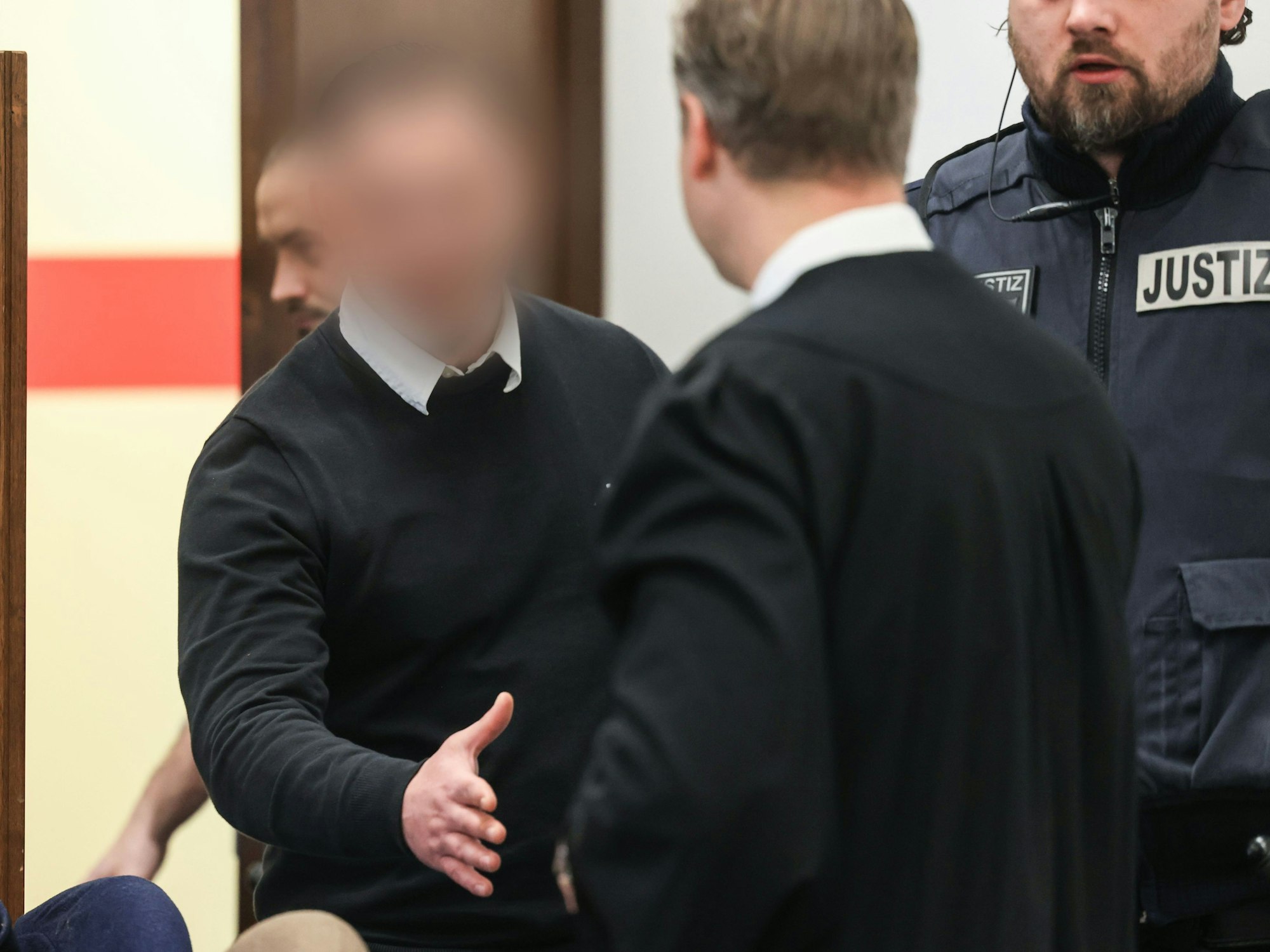Der Angeklagte geht mit ausgestreckter Hand auf seinen Anwalt zu, um ihn zu begrüßen.