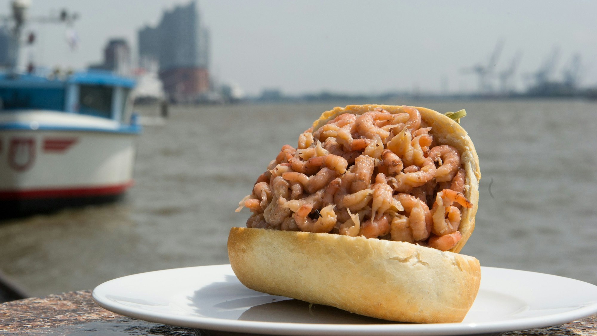 Ein Krabbenbrötchen liegt vor der Silhouette des Hamburger Hafens.