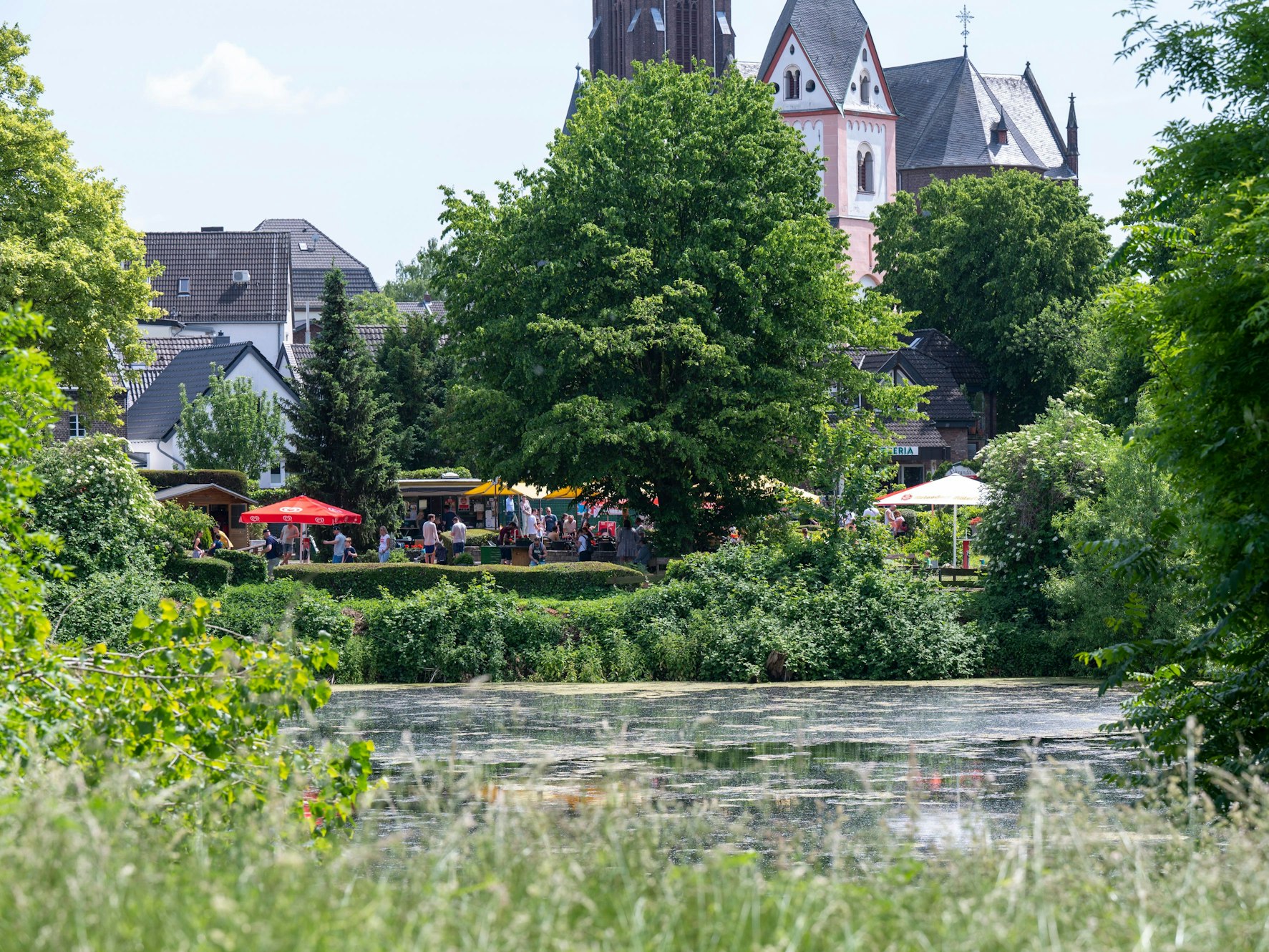 Blick auf einen Teich mit Menschen und Gebäuden im Hintergrund.
