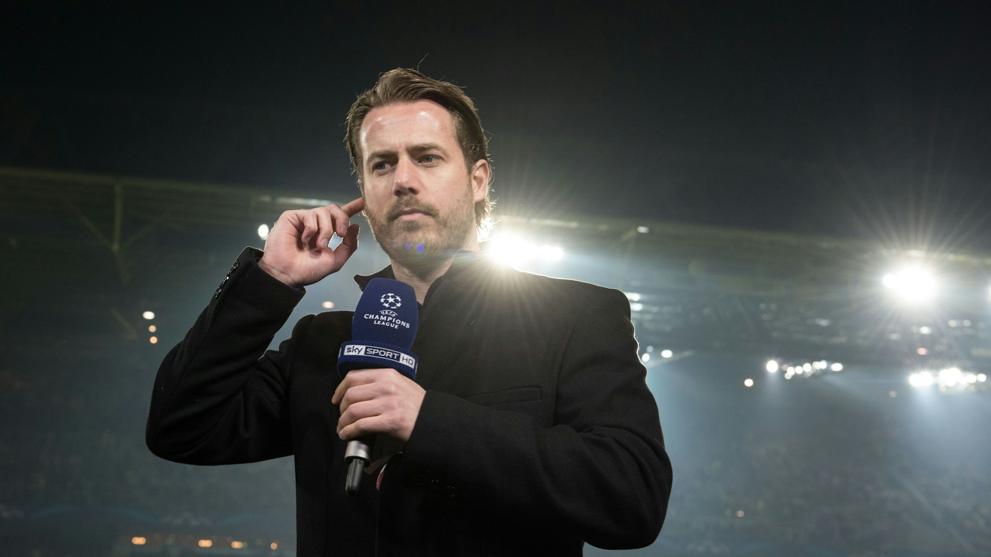 Lars Ricken steht mit einem Mikrophon auf dem Rasen.