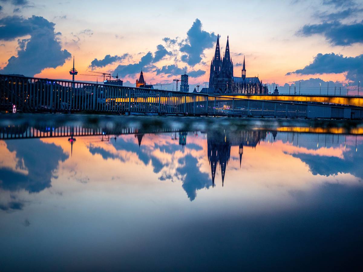 Das Stadtpanorama mit dem Kölner Dom spiegelt sich am Abend kurz vor 22 Uhr in einer Regenpfütze auf der Deutzer Werft.