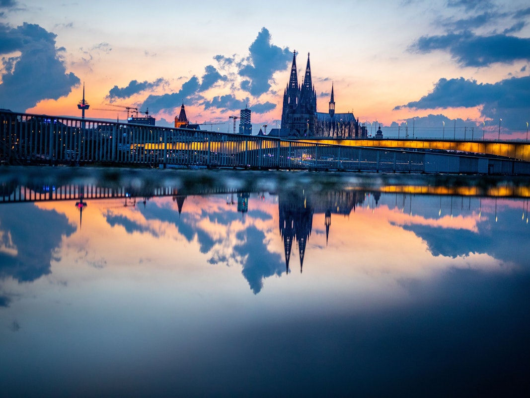 Das Stadtpanorama mit dem Kölner Dom spiegelt sich am Abend kurz vor 22 Uhr in einer Regenpfütze auf der Deutzer Werft.