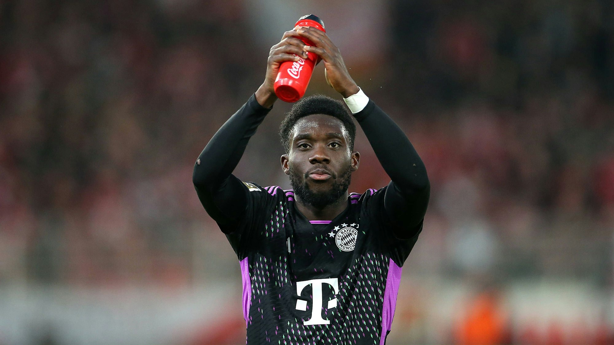 Alphonso Davies klatscht in die Hände und hält dabei seine Trinkflasche fest.
