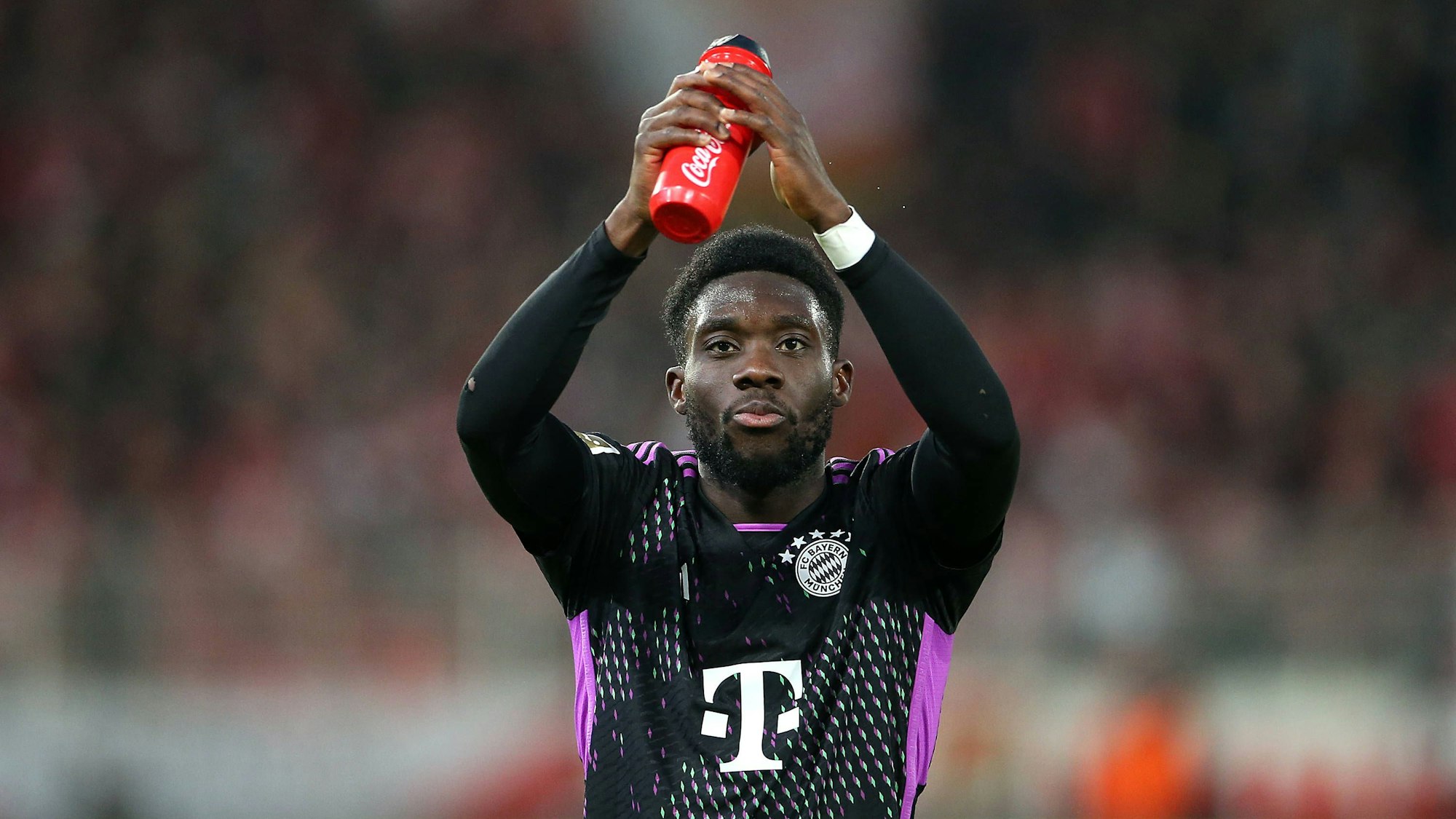 Alphonso Davies klatscht in die Hände und hält dabei seine Trinkflasche fest.