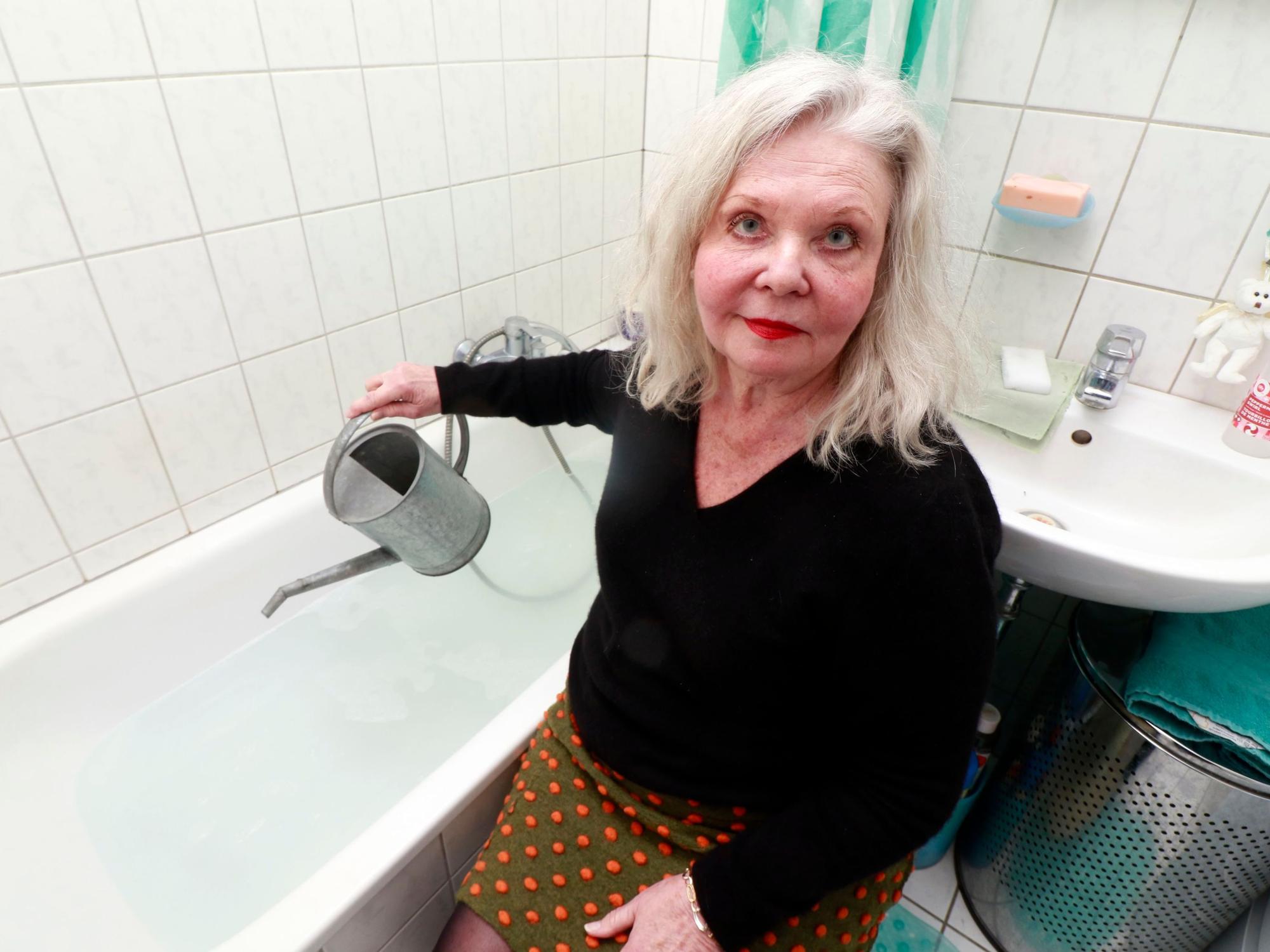 Eine Frau sitzt mit einer Gießkanne neben einer Badewanne.