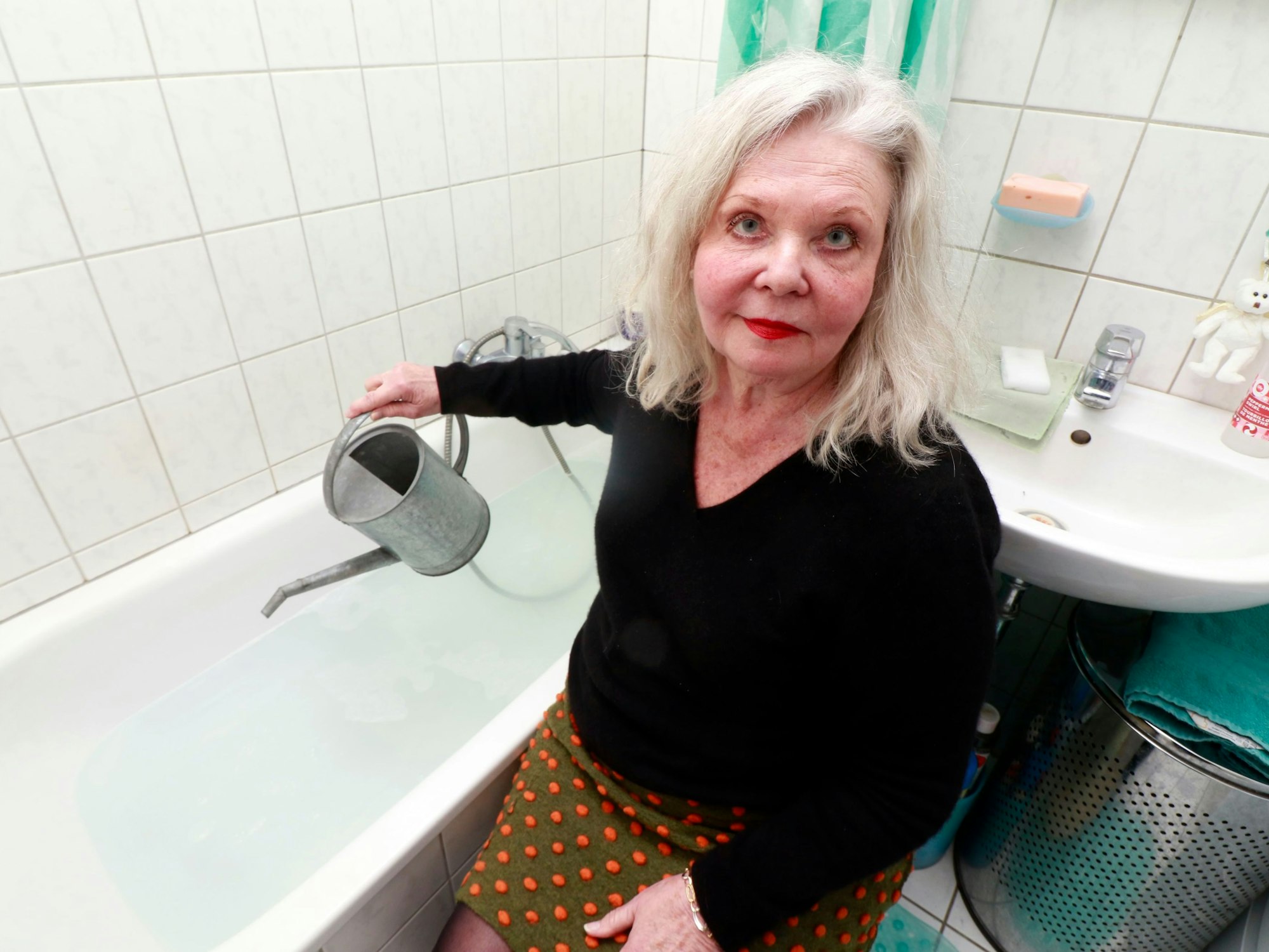 Eine Frau sitzt mit einer Gießkanne neben einer Badewanne.