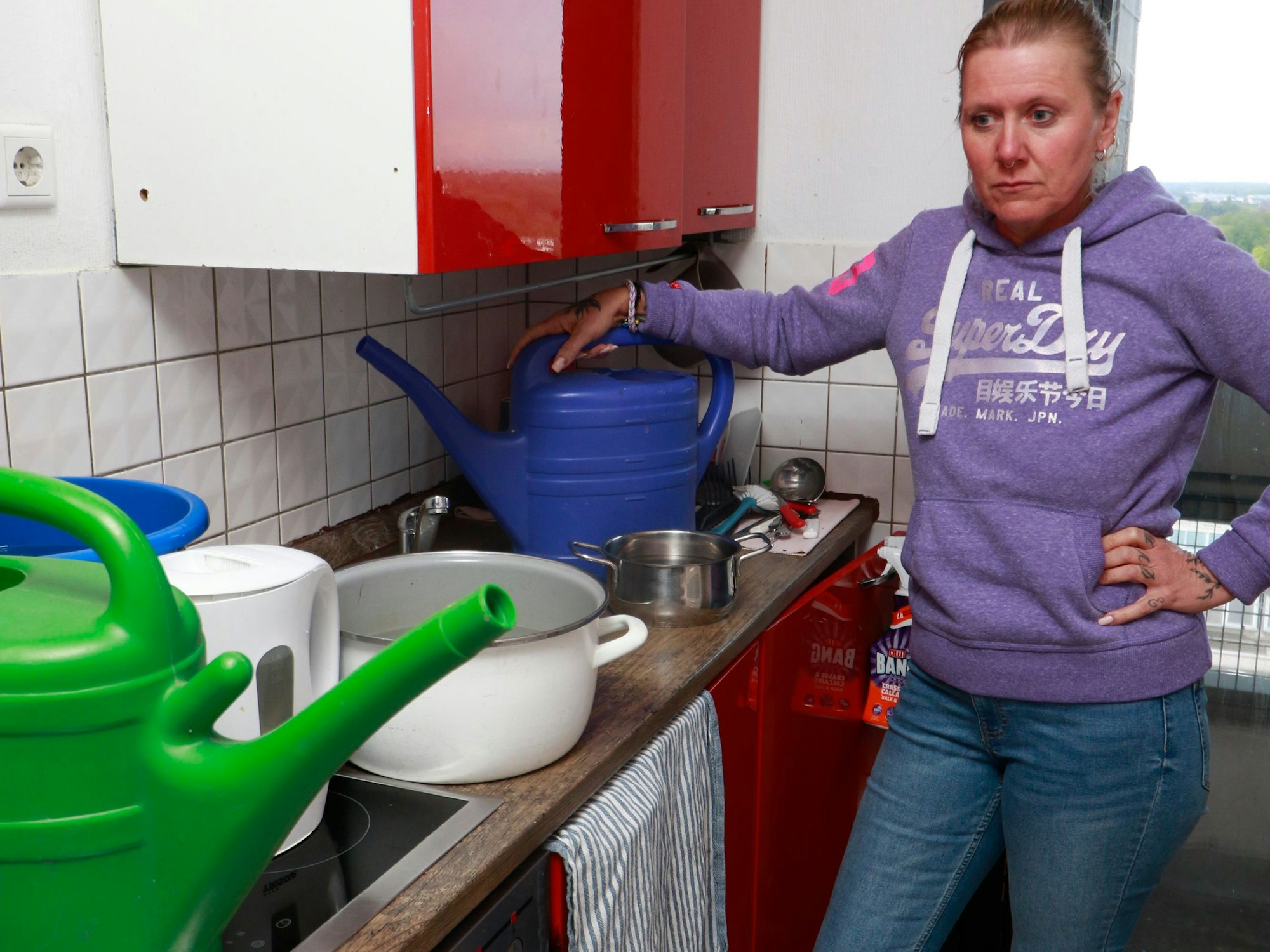 Eine Frau steht vor einer Küche, auf der Gießkannen und Töpfe sind.