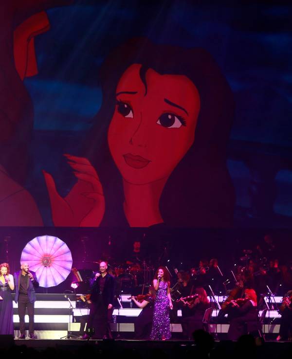 Ein Orchester mit Band und acht Sängern steht auf der Bühne. Im Hintergrund sieht man eine Szene aus Tarzan.