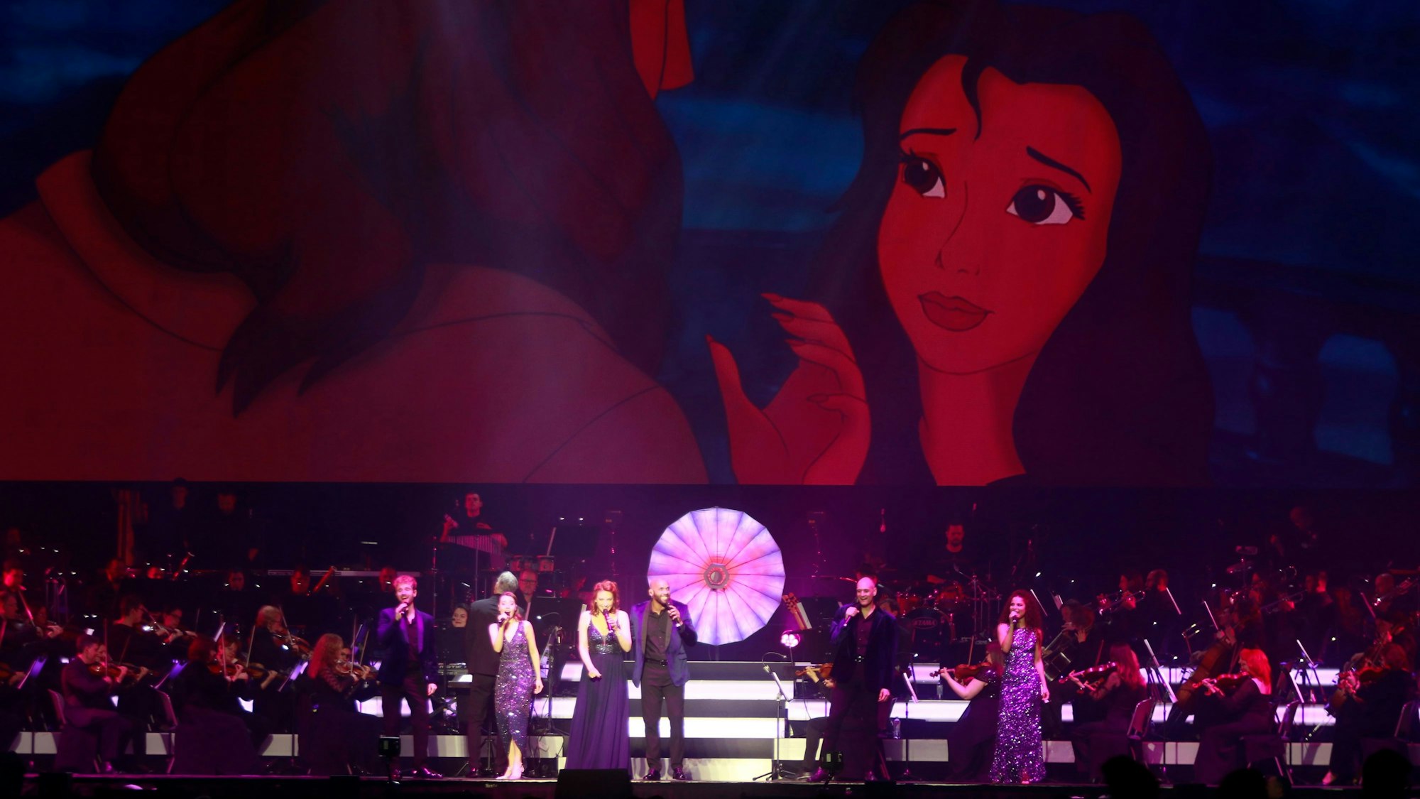 Ein Orchester mit Band und acht Sängern steht auf der Bühne. Im Hintergrund sieht man eine Szene aus Tarzan.