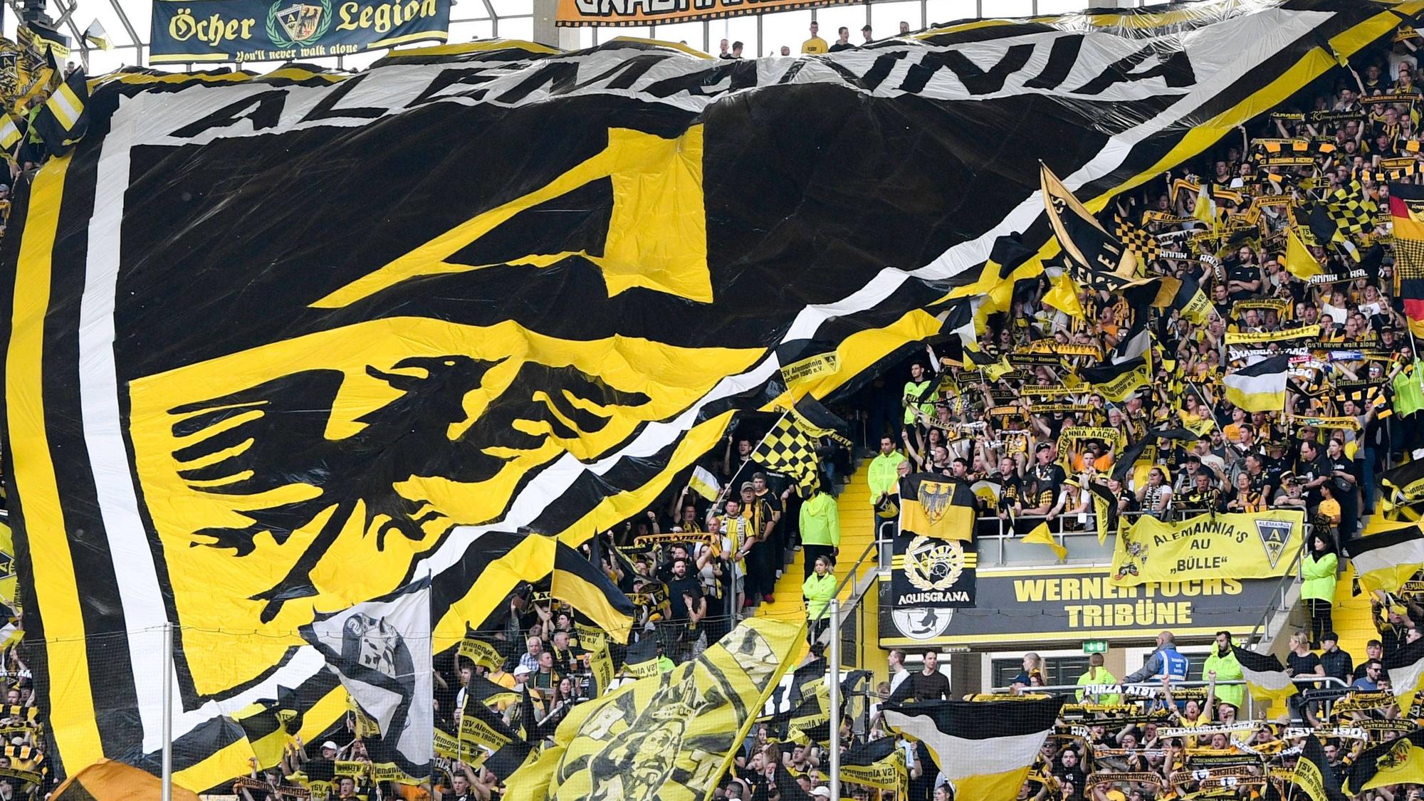 Die Aachener Fankurve hält einen großen Banner mit dem Alemannia-Wappen hoch.
